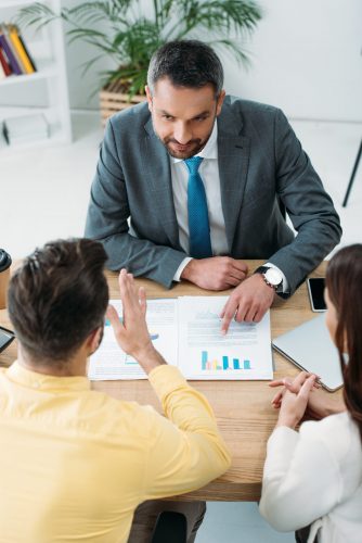 investors sitting at table wile advisor pointing with finger at documents in office